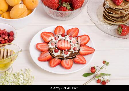 Decorazione di frittelle per una colazione per bambini sotto forma di sole da fragole e panna montata primo piano. Vista laterale. Gustosa colazione estiva Foto Stock