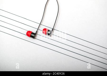 Concetto di giornata mondiale della musica. Un paio di auricolari posizionati su un bastone disegnato su un blocco note che simula note musicali. Foto Stock