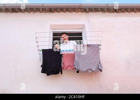 Giovane caucasico appeso i vestiti da una finestra. Concetto di lavanderia. Foto Stock