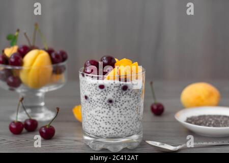 Sana colazione vegana di budino di semi di cia condita con albicocche fresche e ciliegie. Più frutta e cucchiaio d'argento vintage sullo sfondo di legno. Foto Stock