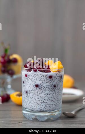 Sana colazione vegana di budino di semi di cia condita con albicocche fresche e ciliegie. Più frutta e cucchiaio d'argento vintage sullo sfondo di legno. Foto Stock