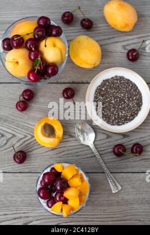 Sana colazione vegana di budino di semi di cia condita con albicocche fresche e ciliegie. Più frutta e cucchiaio d'argento vintage sullo sfondo di legno. Foto Stock