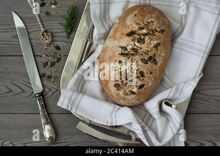 Impasto fresco sfornato pane di segale integrale con semi cosparsi sulla parte superiore. Scuro e moody rustico estetica con sfondo grigio legno, argento vintage Foto Stock