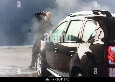 Un uomo lava un'auto in un autolavaggio senza contatto, un uomo lava un'auto marrone, Kaliningrad, Russia, 1 marzo 2020 Foto Stock