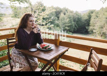 Giovane donna che beve caffè sul balcone della casa di legno Foto Stock