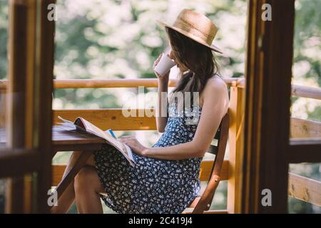 Donna che beve caffè e legga i giornali sul balcone Foto Stock