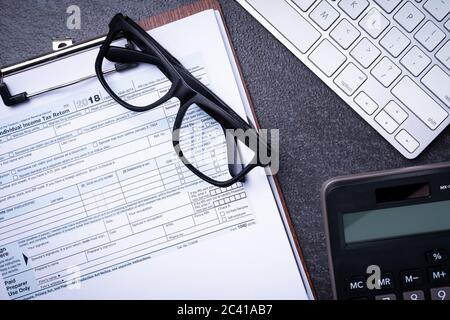 Modulo di rimborso delle imposte sul reddito su una scrivania con monete e calcolatrice Foto Stock