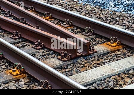 Binari ferroviari giacenti su traversine di calcestruzzo, riempiti tra grandi pezzi di roccia, binari di ricambio al centro della trazione ferroviaria. Foto Stock