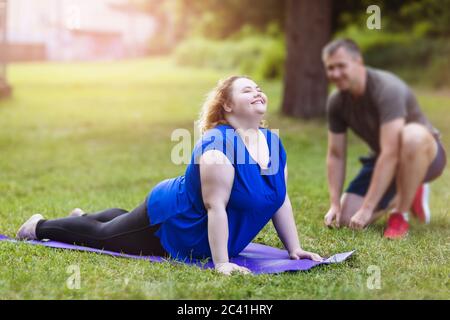 Una giovane bionda di più taglia esegue un esercizio su un terreno sportivo con un allenatore. Concetto di stili di vita sani Foto Stock