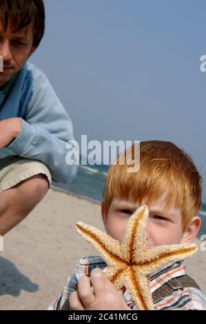 Ragazzo tiene in mano le stelle marine, l'uomo si accovacciano sullo sfondo Foto Stock