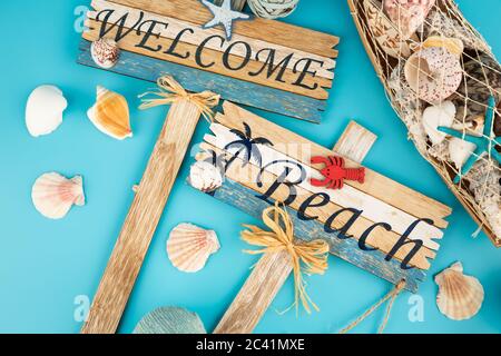 Cartelli in legno danno il benvenuto alla spiaggia e alle conchiglie su sfondo blu. Foto Stock