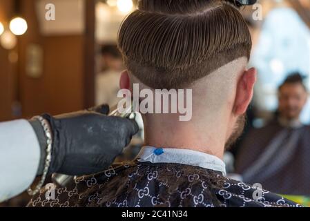 un parrucchiere taglia un giovane ragazzo con un rifinitore per capelli, pettinando i capelli sulla sua testa. Lavoro del maestro nel taglio di capelli degli uomini in un barbiere Foto Stock