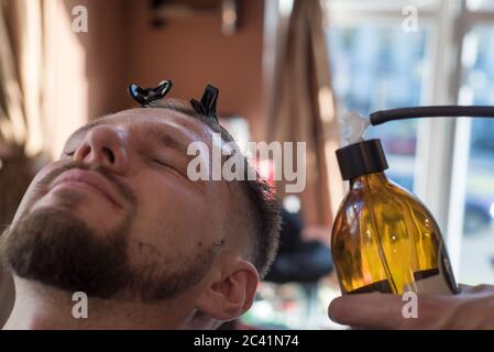 un parrucchiere spruzzando una balsamo dopo aver rasato una barba ad un cliente di un ragazzo giovane bearded di venticinque anni. Al barbiere Foto Stock