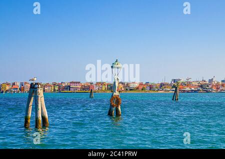 Vista panoramica della laguna di Lusenzo con bastoncini in legno di bricole in acqua e città di Sottomarina con colorati edifici multicolore, cielo blu in estate, Regione Veneto, Italia settentrionale Foto Stock