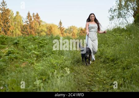 Donna brunetta a piedi con cane in parco in estate Foto Stock