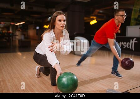 Una bella coppia caucasica che lancia palle sulla pista da bowling. Fidanzata e ragazza al bowling club Foto Stock