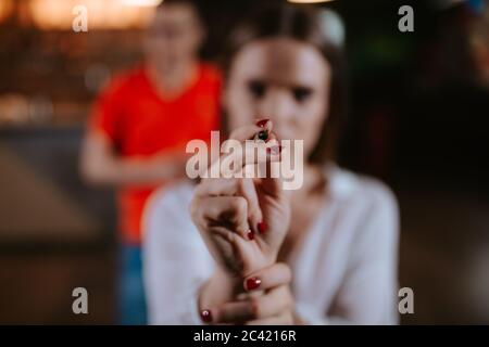 Primo piano di una mano di una ragazza che lancia una freccia su una tavola di freccette Foto Stock