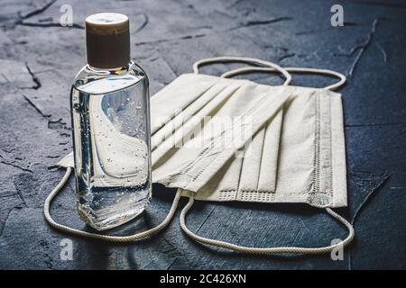 Gel idroalcolico o flacone di gel antisettico per le mani e maschere facciali bianche. Protezione sanitaria di base contro il virus del coronavirus o del covid-19. Foto Stock