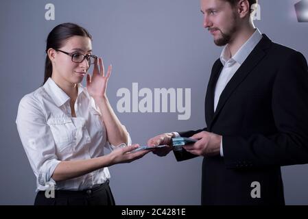 Ritratto di due giovani imprenditori. Una donna d'affari toglie i suoi occhiali, guarda tristemente al piccolo stipendio che il suo capo mette in mano. Studio Foto Stock