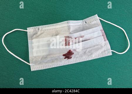 Maschera facciale o chirurgica usata con macchie di sangue, sfondo verde. Dispositivi di protezione individuale durante il periodo di un pandemi di infezione da coronavirus Foto Stock