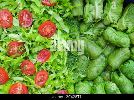 Involtini di carne di orache verdi, foglie di insalata e fette di pomodoro di ciliegia rossa, impaccate insieme in pentola prima di cucinare in forno Foto Stock