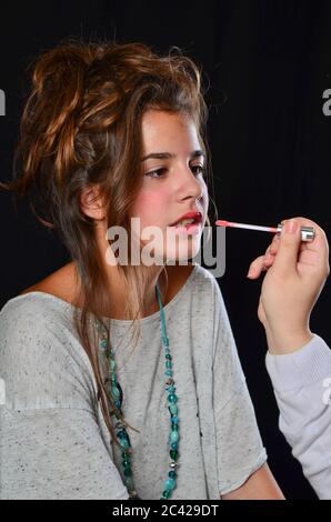 Trucco professionale di ragazza bruna adolescente durante la preparazione per la sessione di foto, studio girato su sfondo nero Foto Stock