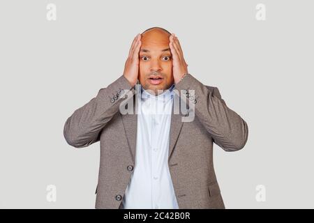 Un uomo afro-americano eccitato, sorpreso, aprendosi la bocca a sorpresa, tenendo la mano sulla testa, scioccato da notizie inaspettate. Espressione ed emozioni del viso umano. Foto Stock