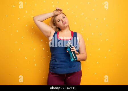 Fat girl fa palestra a casa. Espressione stanca. Sfondo giallo Foto Stock