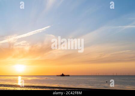 Il tramonto in un cielo parzialmente nuvoloso sul mare con i resti della testa del molo di Herne Bay sizati all'orizzonte. Il sole affonda in un cielo arancione e blu. Foto Stock