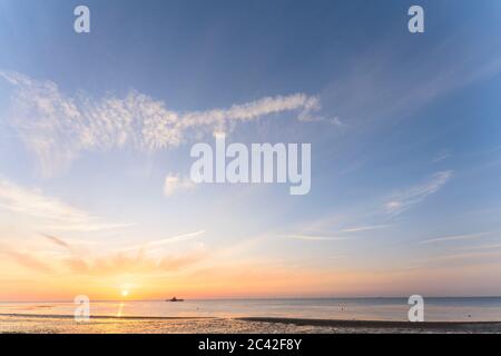 Il tramonto in un cielo parzialmente nuvoloso sul mare con i resti della testa del molo di Herne Bay sizati all'orizzonte. Il sole affonda in un cielo arancione e blu. Foto Stock