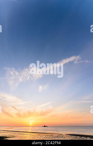 Il tramonto in un cielo parzialmente nuvoloso sul mare con i resti della testa del molo di Herne Bay sizati all'orizzonte. Il sole affonda in un cielo arancione e blu. Foto Stock