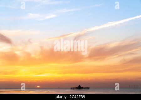 Il tramonto in un cielo parzialmente nuvoloso sul mare con i resti della testa del molo di Herne Bay sizati all'orizzonte. Il sole affonda in un cielo arancione e blu. Foto Stock