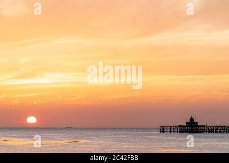 Il tramonto in un cielo parzialmente nuvoloso sul mare con i resti della testa del molo di Herne Bay sizati all'orizzonte. Il sole affonda in un cielo arancione e blu. Foto Stock