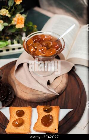 Confitto di prugna gialla in un vaso di vetro su un asse di legno, con due fette di pane tostato Foto Stock