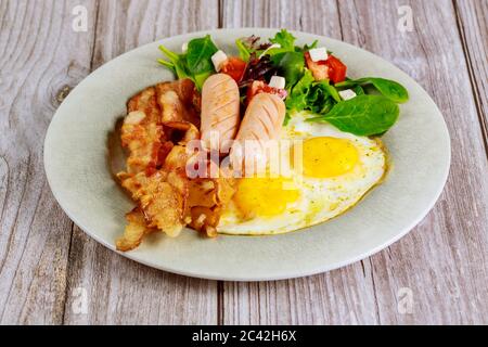franche di pollo, uova fritte, pancetta e insalata su tavolo di legno per la colazione. Foto Stock