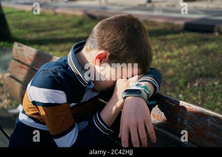 bambino su una panchina copre il viso con il braccio e piange Foto Stock