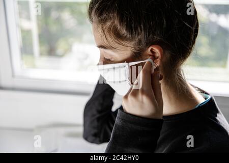 Da parte giovane donna seamstress seduta cercando su una maschera appena autofmade in officina a casa Foto Stock