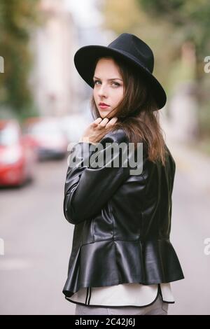 Ritratto di giovane donna esterna con cappello nero e pelle giacca Foto Stock