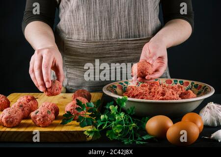 La cuoca forma la carne macinata per preparare polpette fatte in casa condendole con spezie diverse per il sapore. Foto Stock