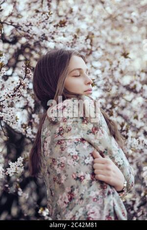 Giovane donna in piedi di fronte all'albero dei fiori di ciliegio Foto Stock