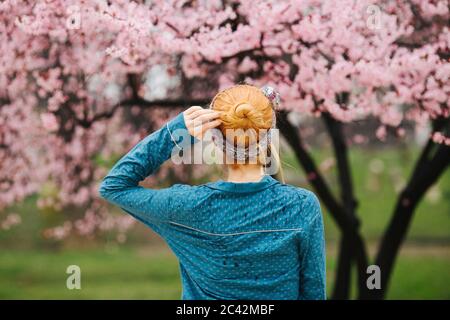 Vista posteriore della donna rossa in piedi di fronte al ciliegio albero fiorito Foto Stock