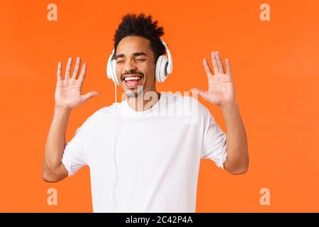 Una qualità audio fantastica. Carefree felice, sorridente afro-americano in t-shirt bianca con canti e gesti come godersi musica, ascoltare via Foto Stock