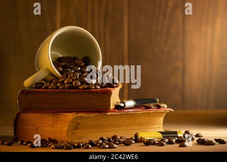 Chicco di caffè nella tazza bianca e libro vintage impilamento sul tavolo di legno nella luce del mattino. Foto Stock