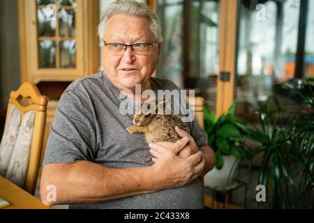 Sand am Main, Germania. 15 giugno 2020. Karl-Heinz Mahr tiene il giovane campo lepre 'HASI' tra le sue braccia. Il suo cane aveva rintracciato la lepre di campo nel giardino della famiglia nel distretto di Schweinfurt, ipotermico e affamato. Il coniglio fu curato dalla famiglia, ma poi, su istruzioni di un veterinario, fu preso in cura di un centro di soccorso e poi morì. Credit: Nicolas Armer/dpa/Alamy Live News Foto Stock