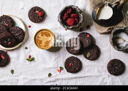 Biscotti salati di brownie al cioccolato fondente fatti in casa decorati da lamponi freschi e secchi, con scaglie di sale, bacche, menta, latte e tazza di caffè Foto Stock