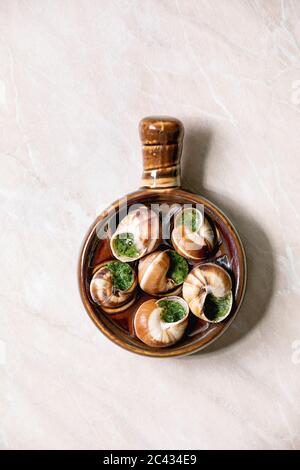 Escargots de Bourgogne - lumache con burro alle erbe, piatto gourmet, in tradizionale padella ceramica su sfondo di marmo rosa. Piatto, spazio Foto Stock