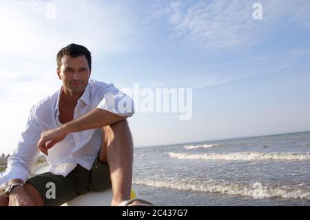 Uomo seduto sulla spiaggia Foto Stock