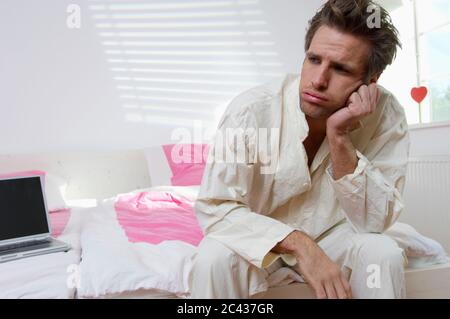 Annoiato uomo di mezza età in pigiama si siede sul letto Foto Stock