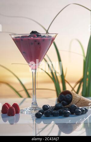 Bicchiere Martini con frullato di frutta e more circondato da mirtilli, lamponi e un cono di ghiaccio su uno sfondo sfocato. Vacanze e h Foto Stock