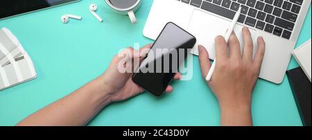 Foto a testa di freelance maschile con smartphone e tastiera a destra sul laptop Foto Stock